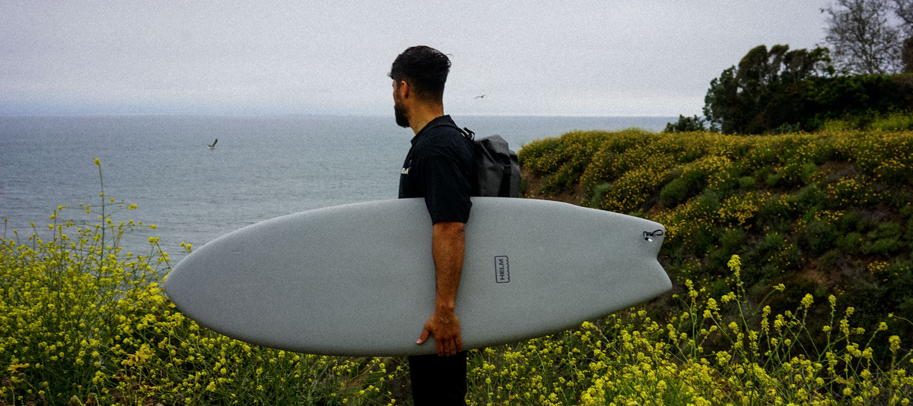 Surfer holding a HELM Performance Fish surfboard at the beach, checking the waves — best small wave surfboards 2026